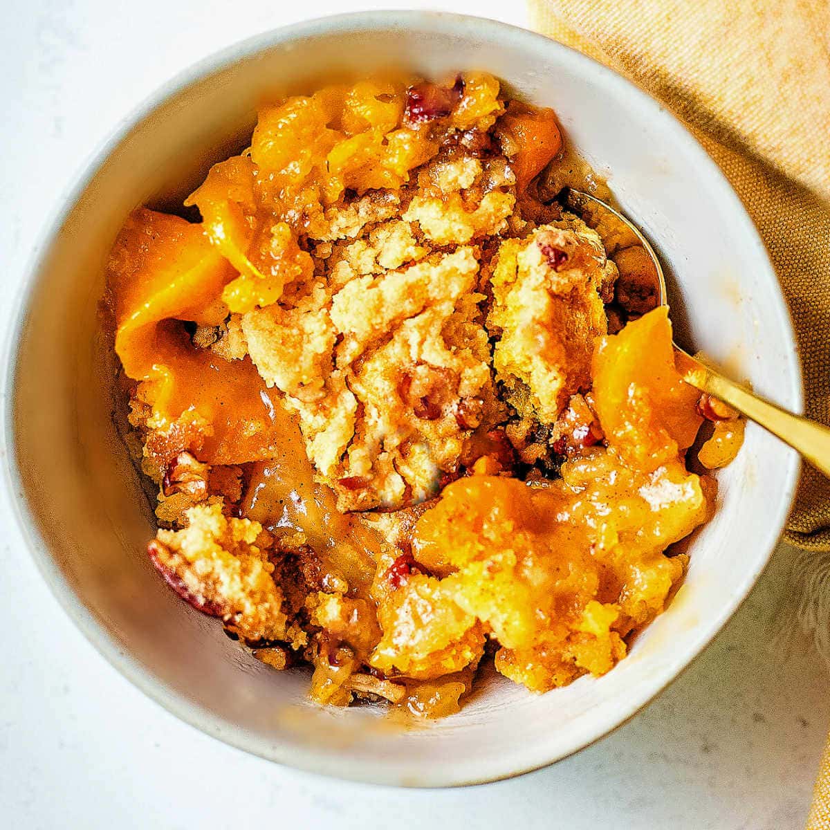 Peach Dump Cake in a bowl with a gold spoon.