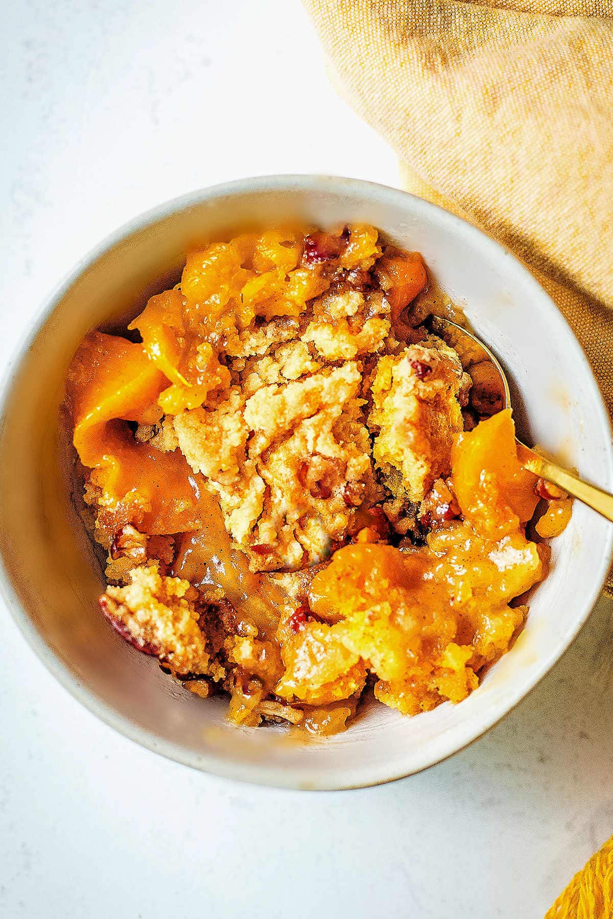 Portion of peach dump cake in a bowl with a spoon.