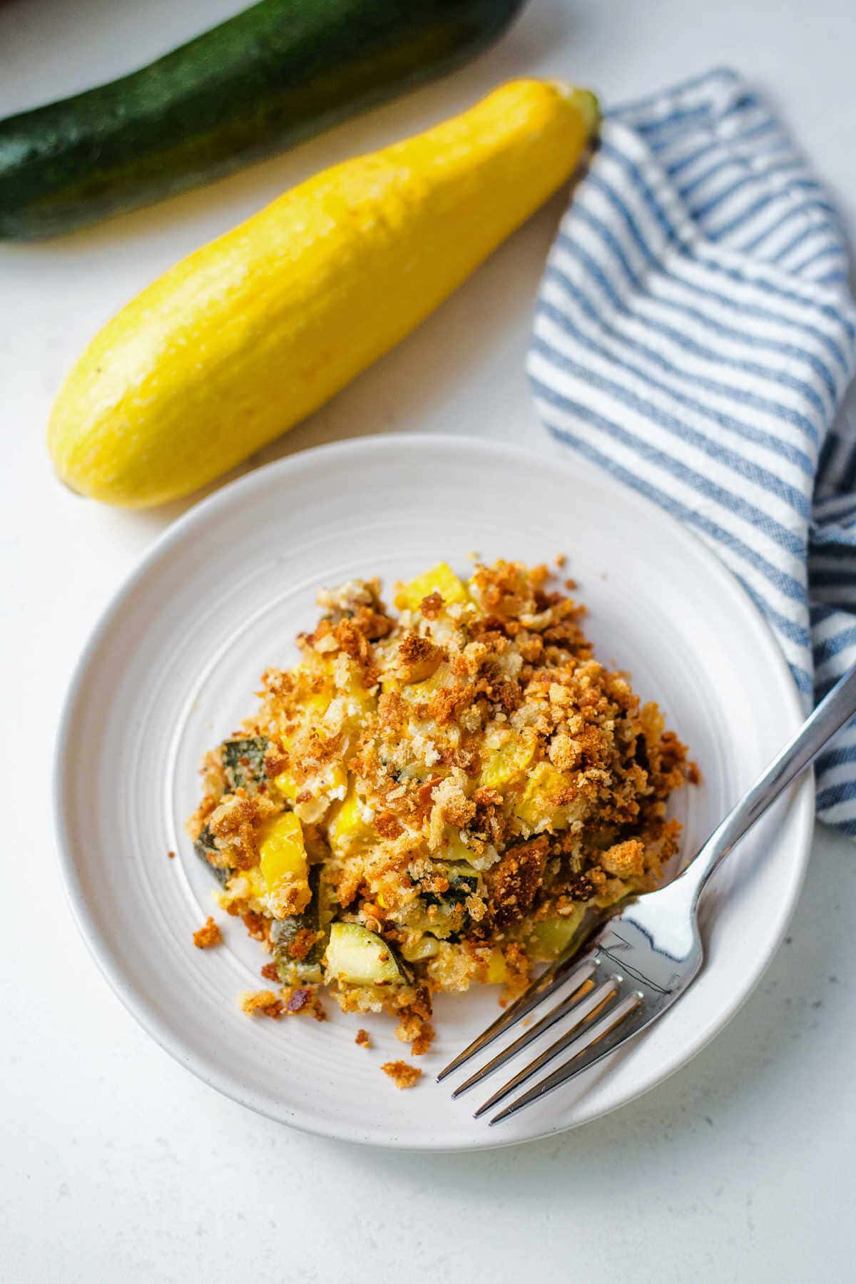 Portion of summer squash casserole on a white plate with a fork.