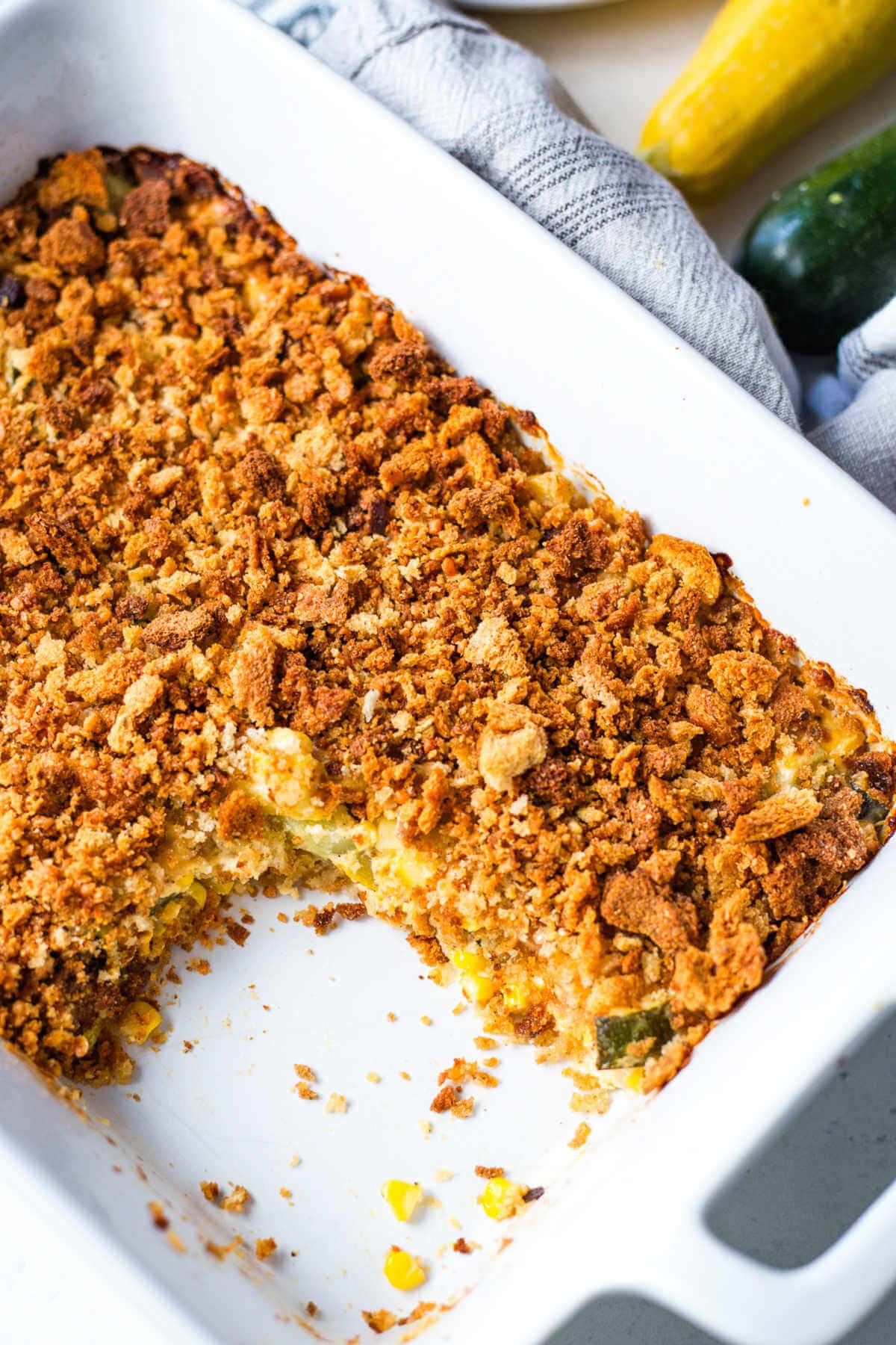 Summer squash casserole in a white baking dish with a portion missing.