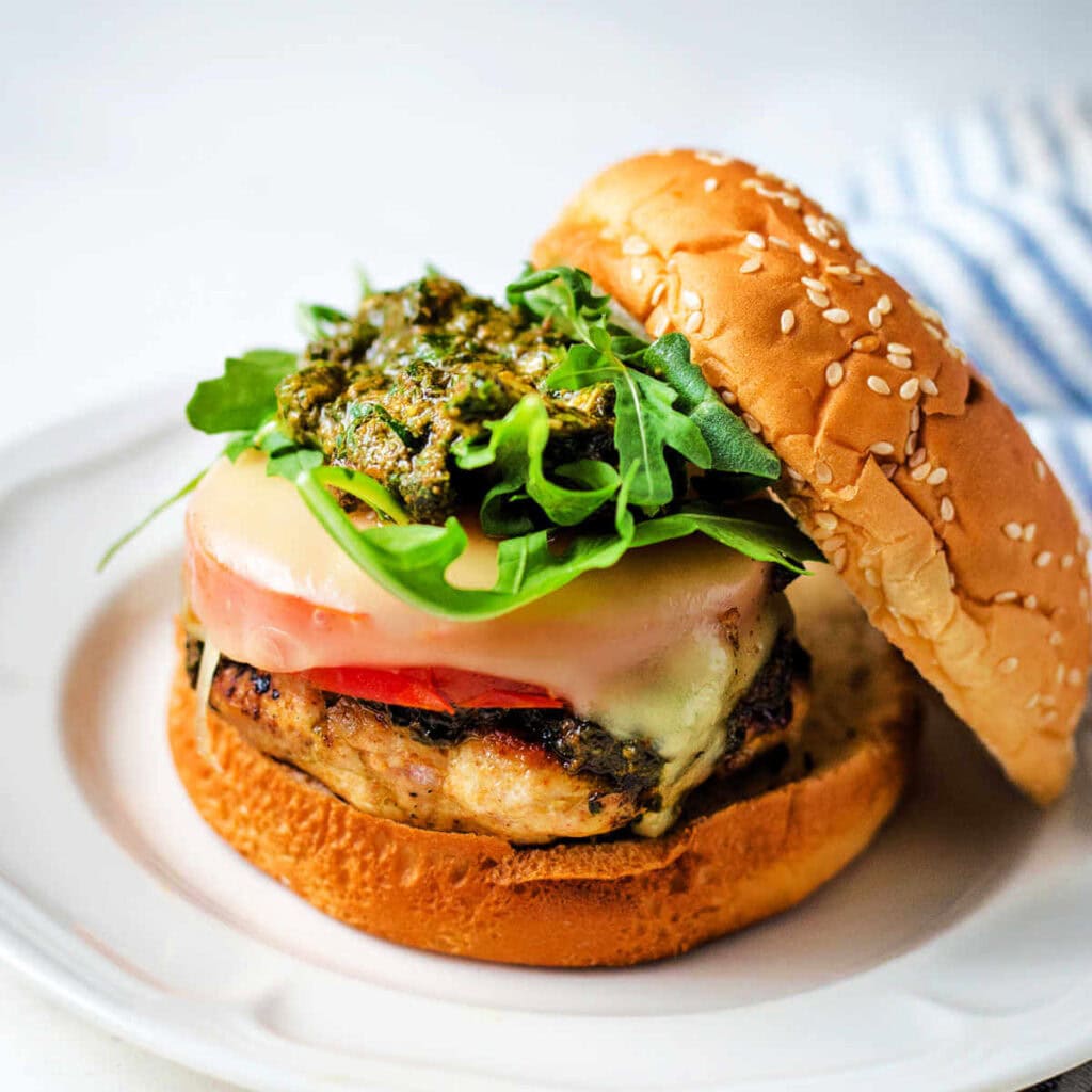 Chicken Burger with sliced tomato, mozzarella cheese, pesto, and arugula on a sesame seed bun.