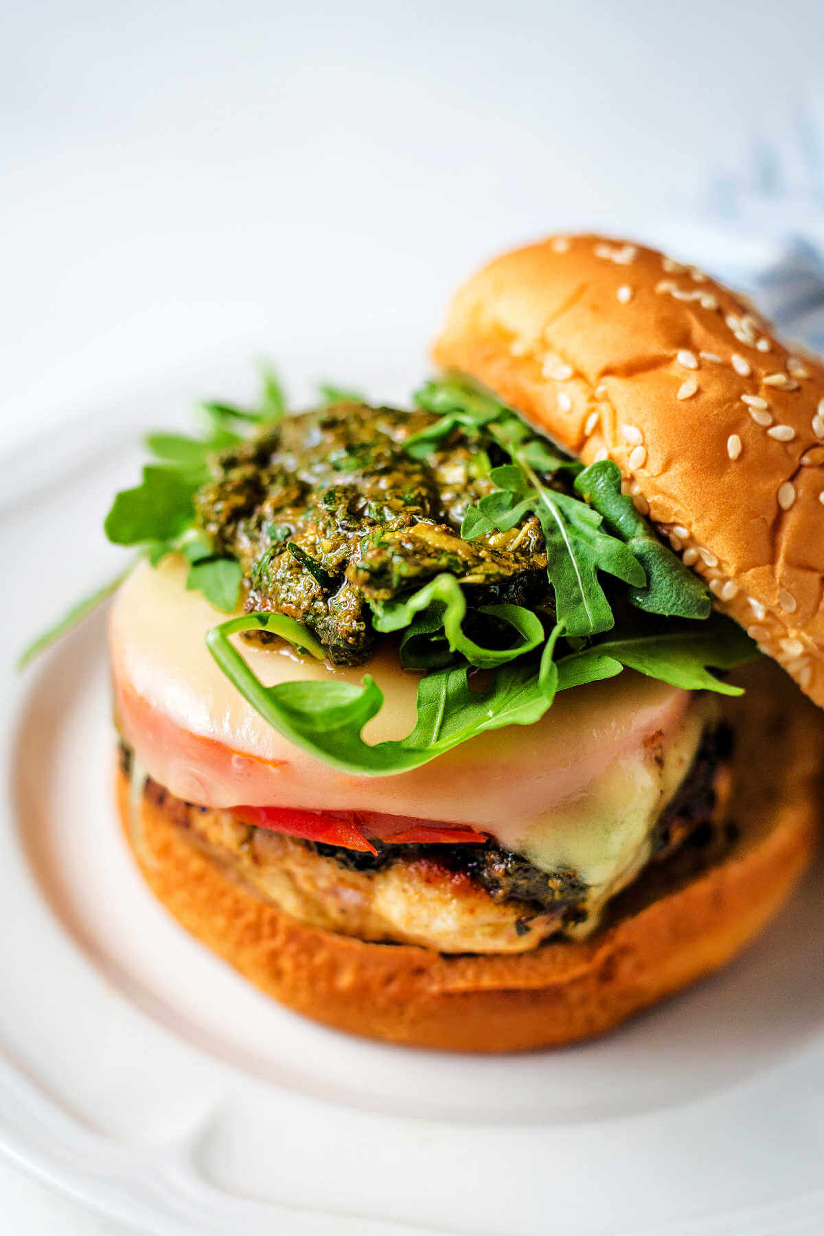 Caprese-style ground chicken burgets with tomato, mozzarella, pesto, and arugula on top.
