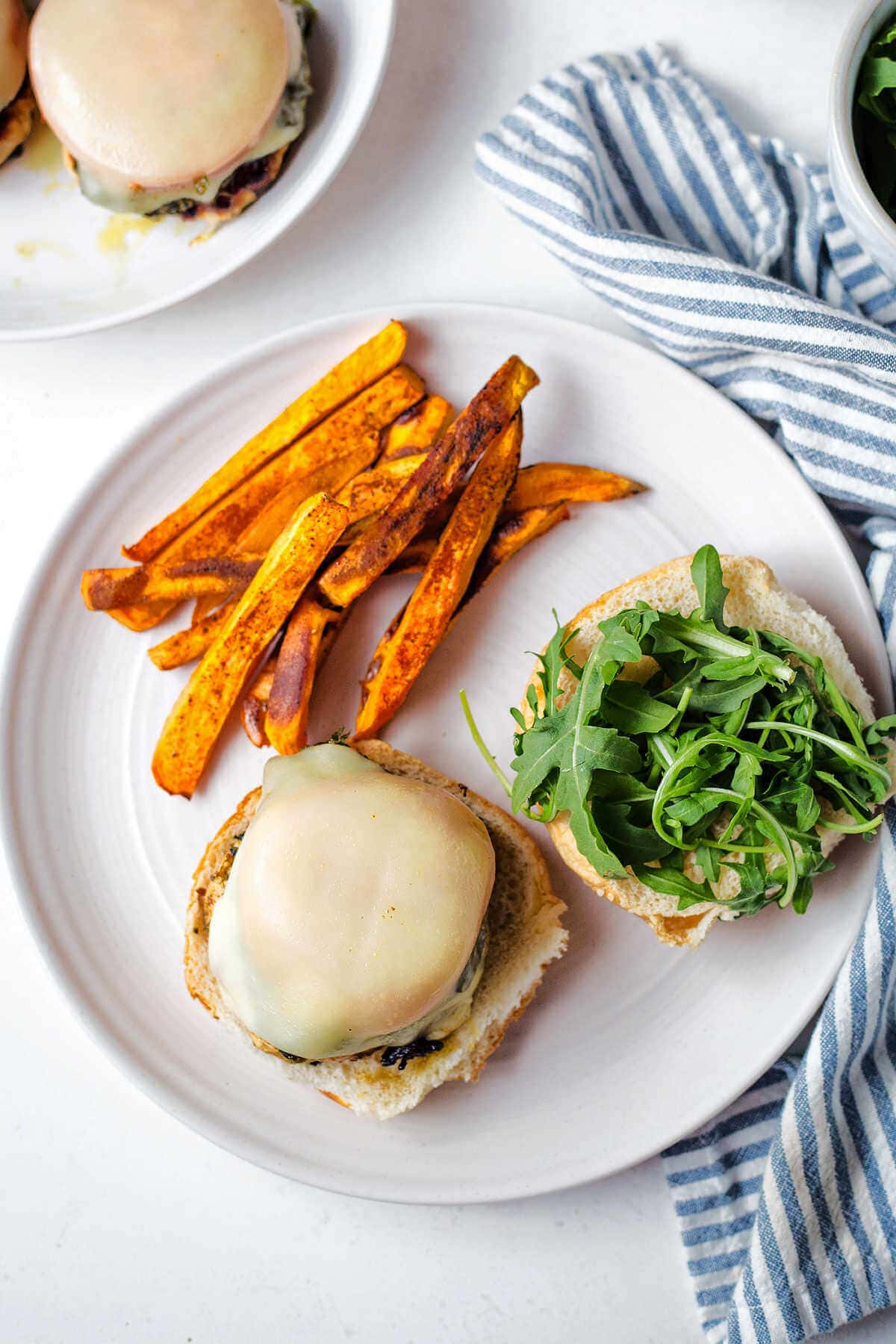 Open faced chicken burger served with arugula and sweet potato fries.