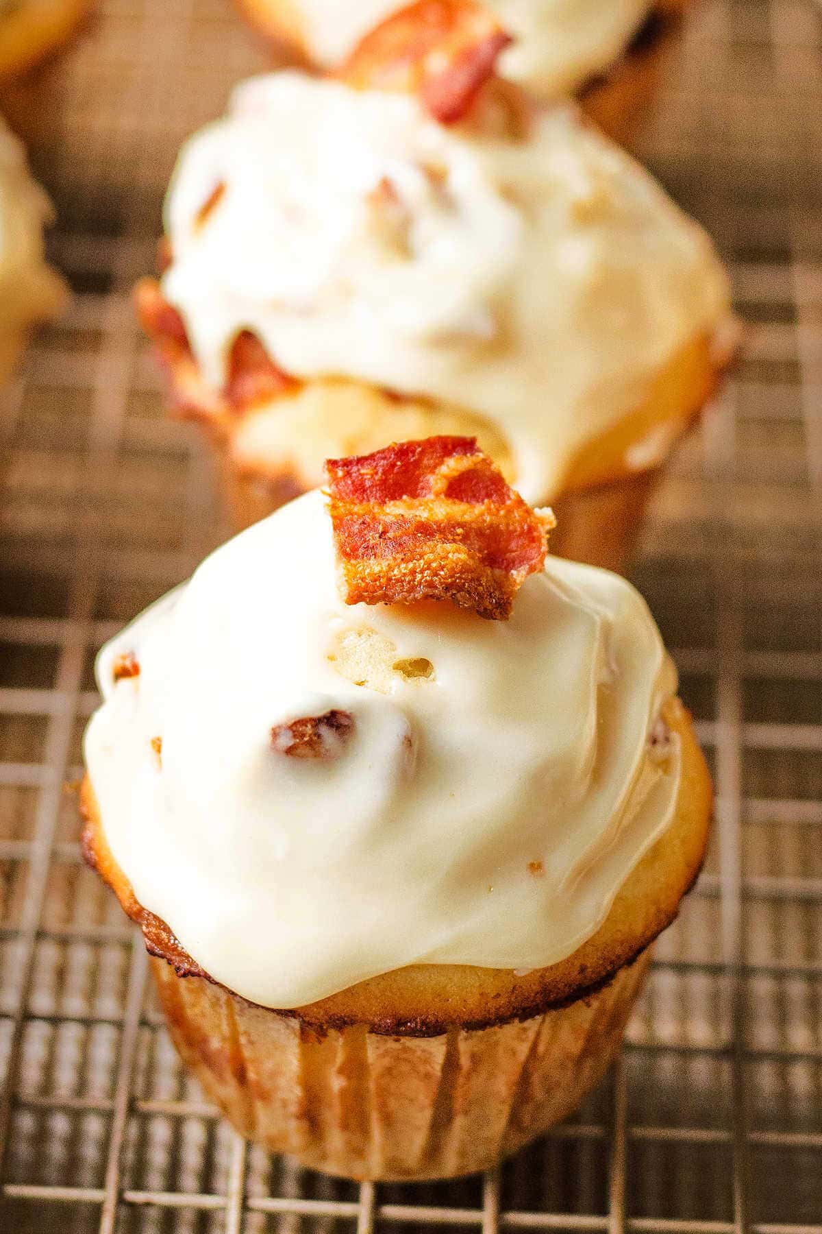 Maple-glazed bacon muffin on a cooling rack with maple glaze and a piece of bacon on top.