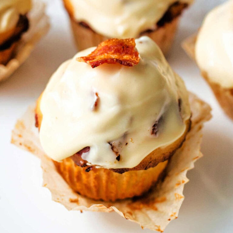 A Maple-Glazed Bacon Muffin garnished with a bacon piece on a paper cupcake liner.
