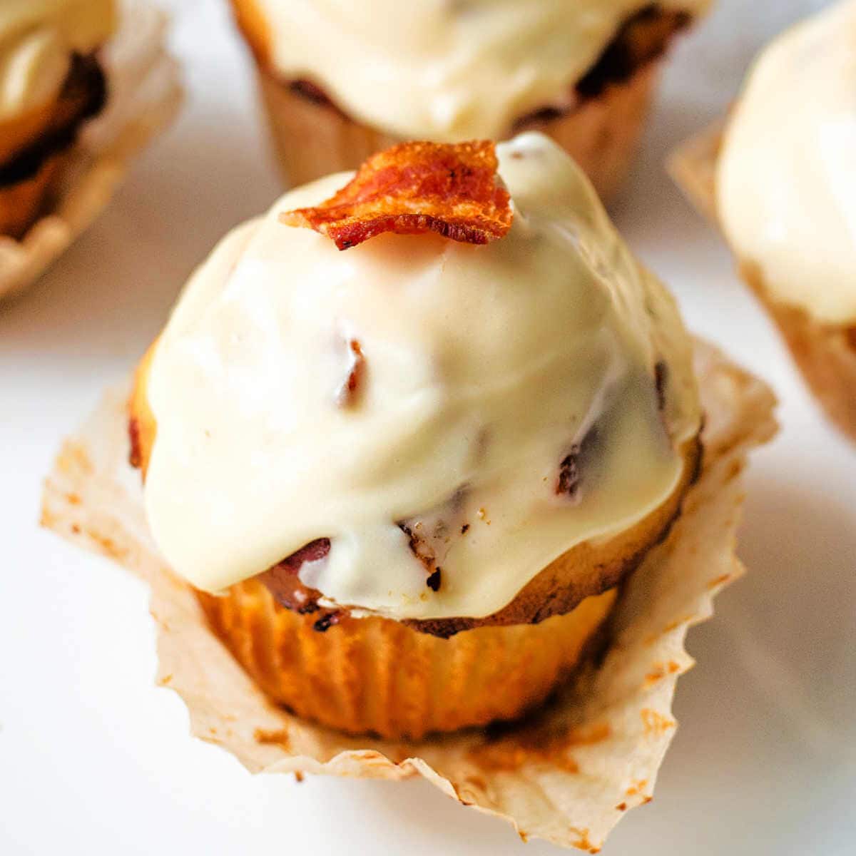 A Maple-Glazed Bacon Muffin garnished with a bacon piece on a paper cupcake liner.