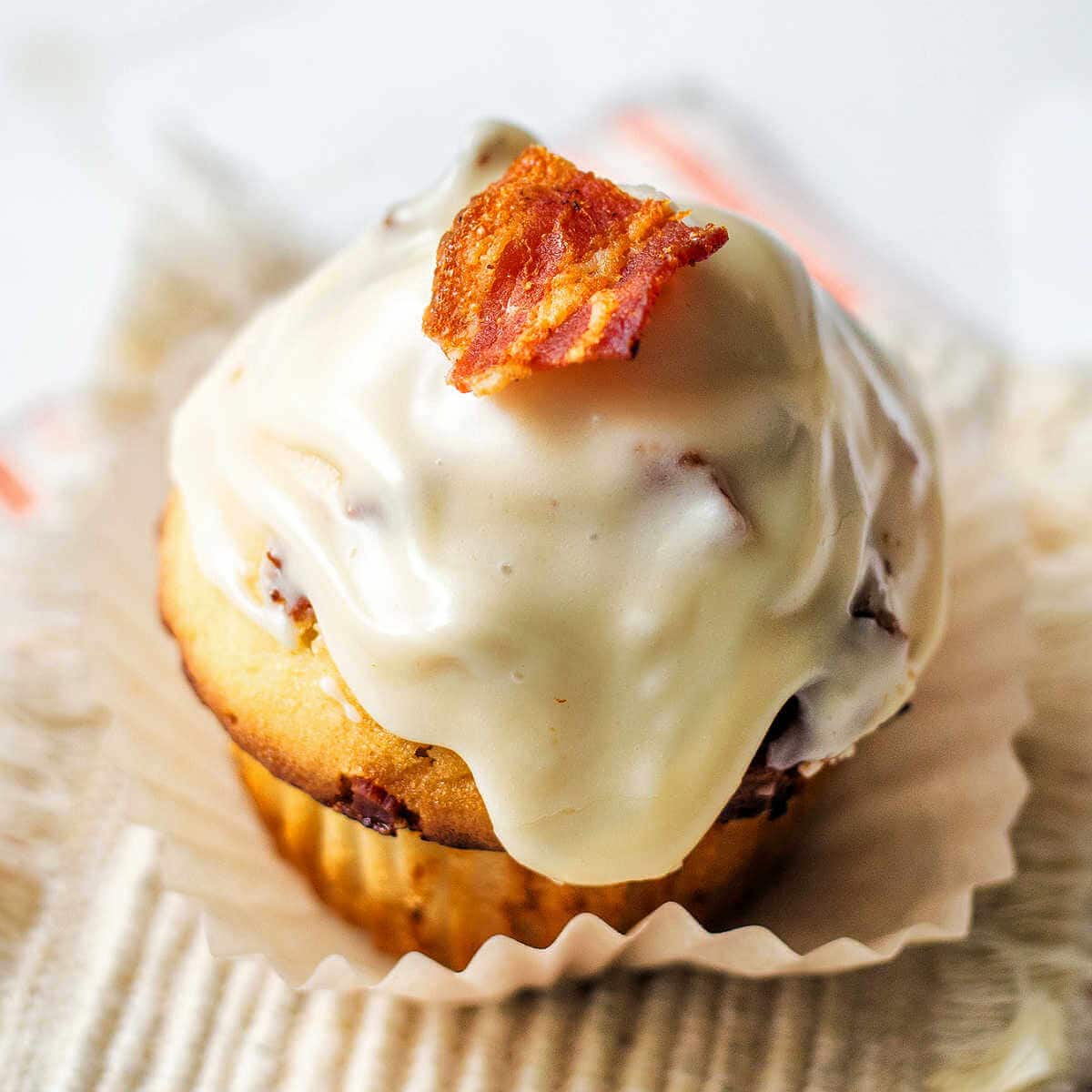 A Maple-Glazed Bacon Muffin garnished with a bacon piece on a paper cupcake liner.