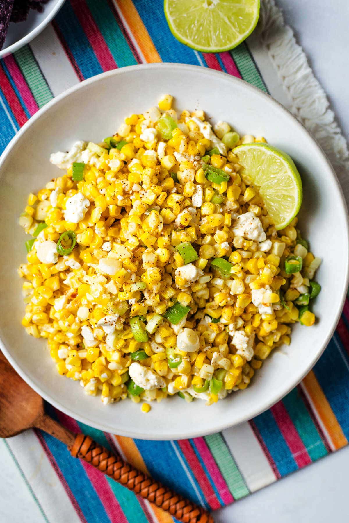 Mexican corn salad served in a white bowl with a lime wedge on the side.
