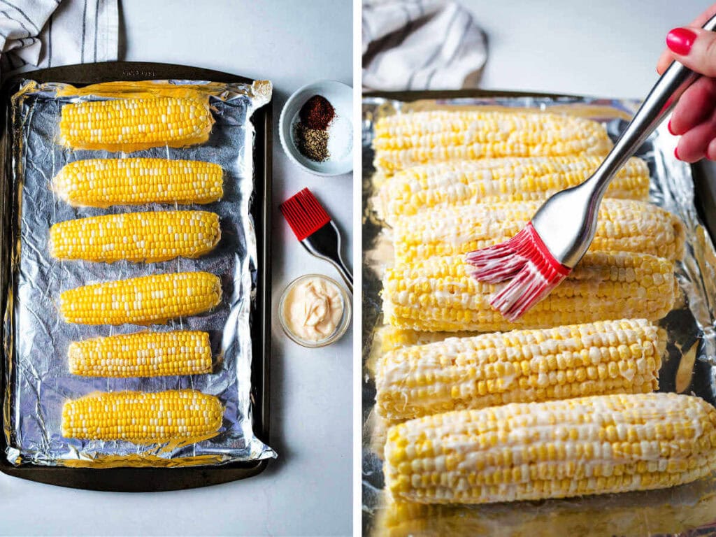 Corn on the cob on a sheet pan being brushed with mayo.