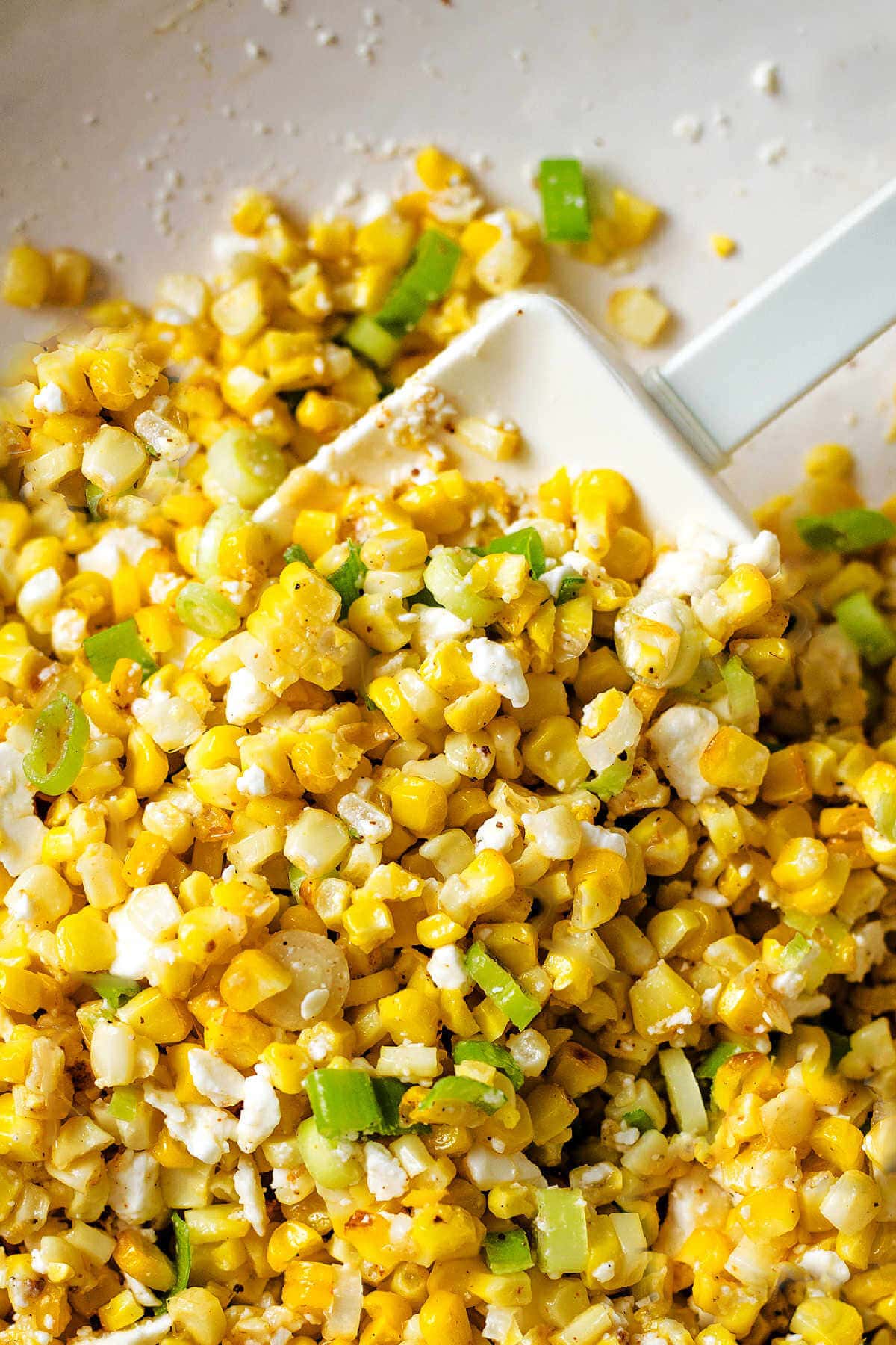 Mexican corn salad in a bowl with a rubber spatula after mixing.