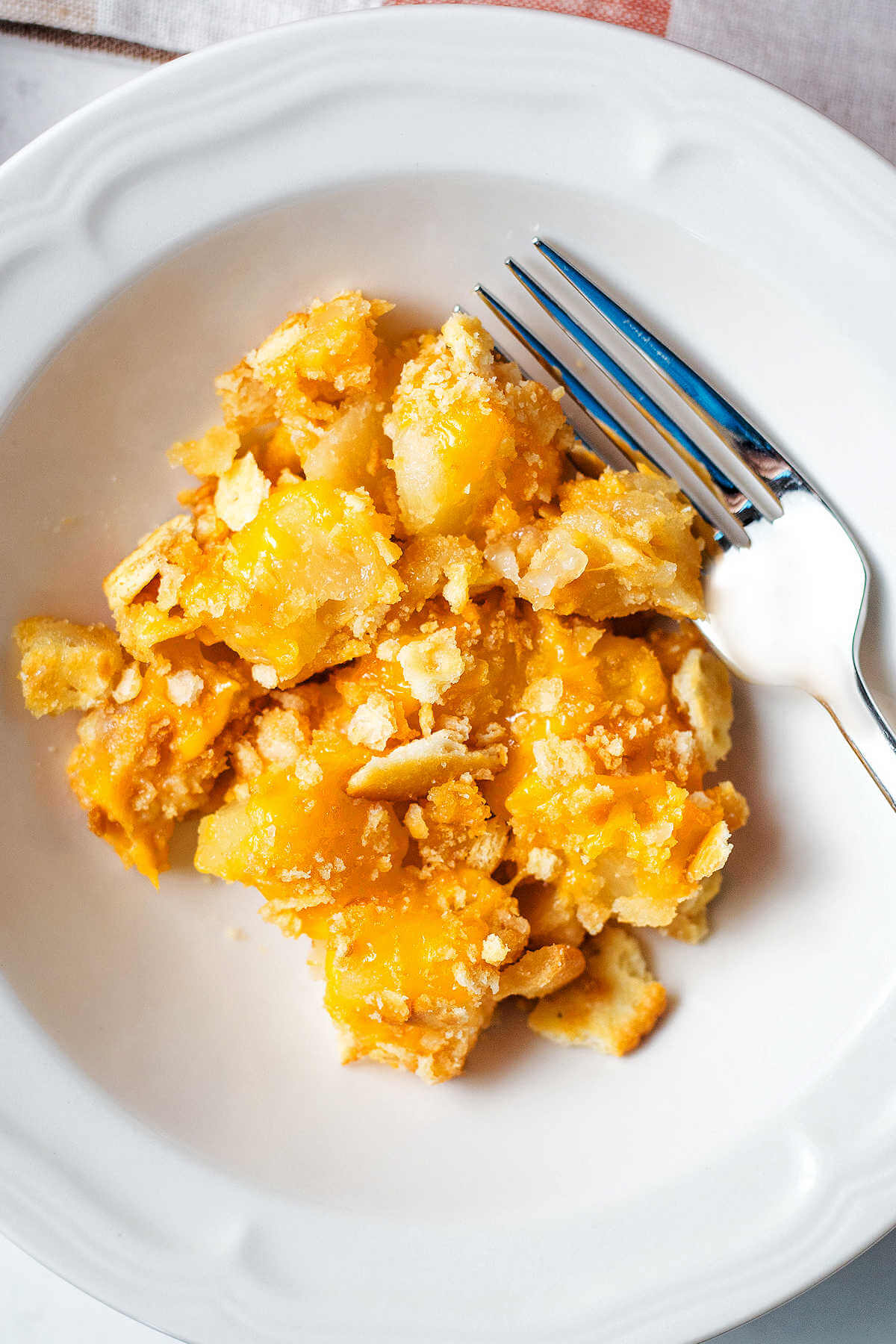 Portion of pineapple casserole served in a white bowl with a fork.