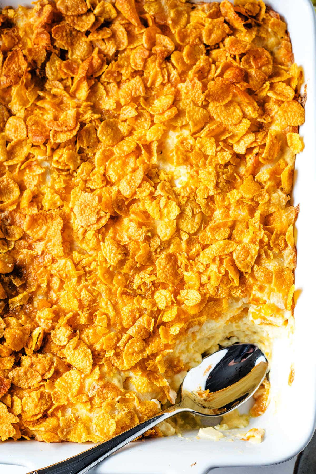 Funeral potatoes in a baking dish with a portion missing.