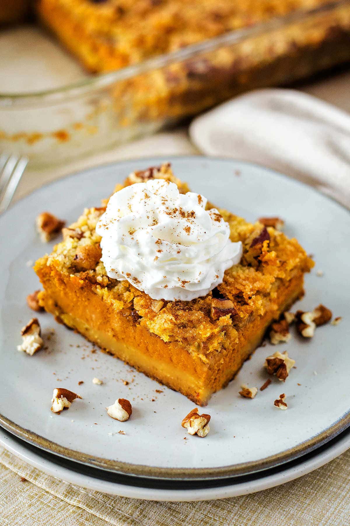 Slice of pecan dump cake with pecan crumble on a plate topped with whipped cream.