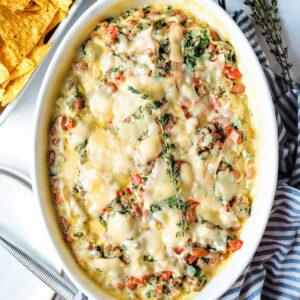 Cheesy sausage dip with beans and spinach in a baking dish.