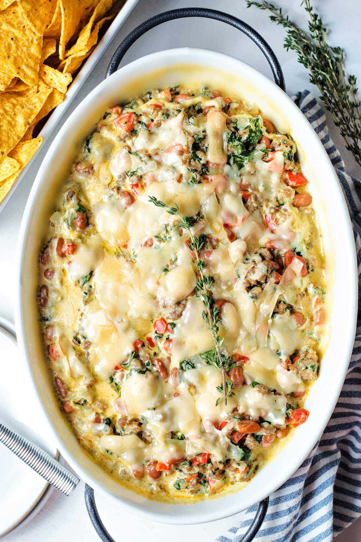 Overhead shot of finished sausage dip with beans and spinach in a baking dish.