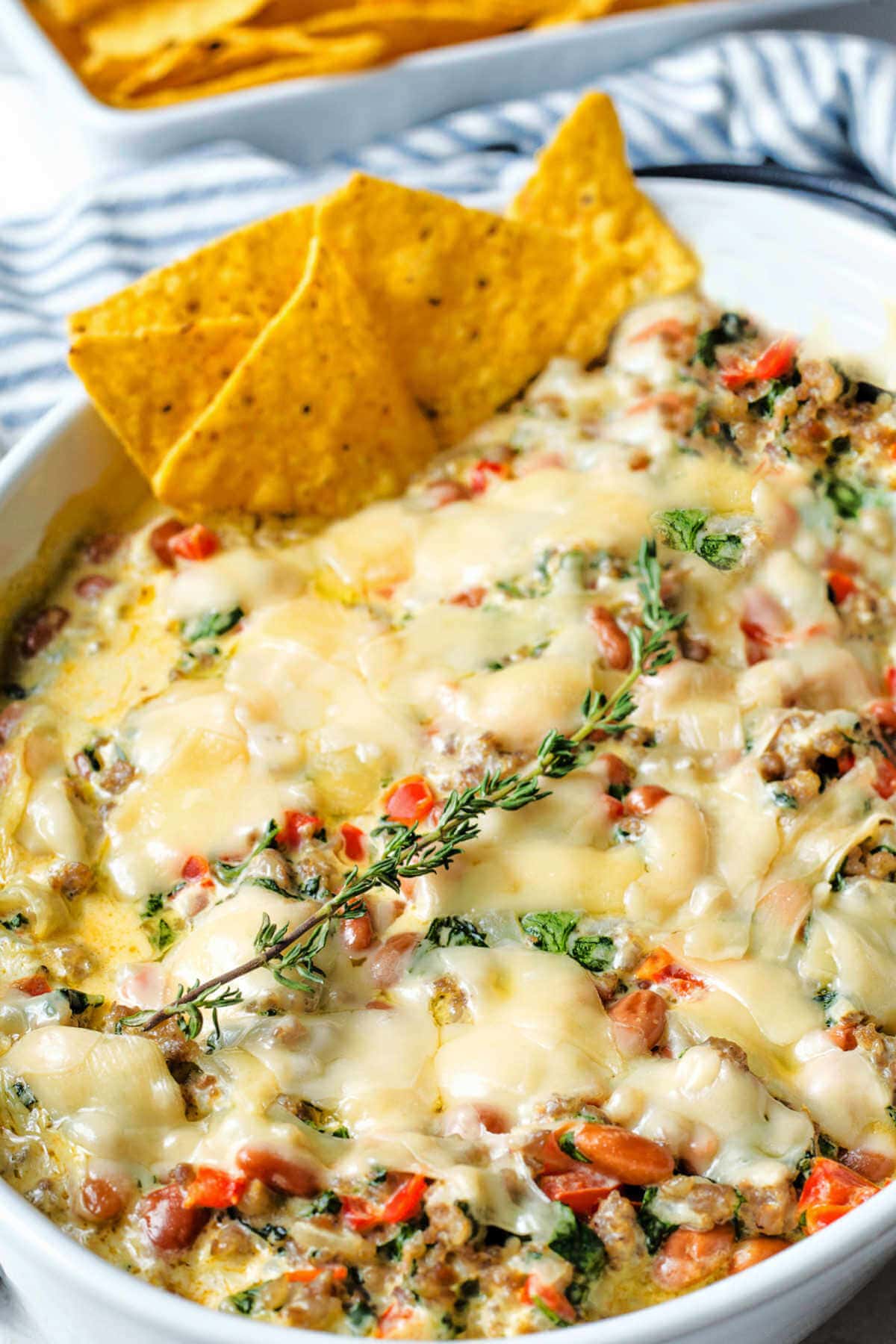 Side view of sausage dip with melted parmesan on top and some chips in the side.