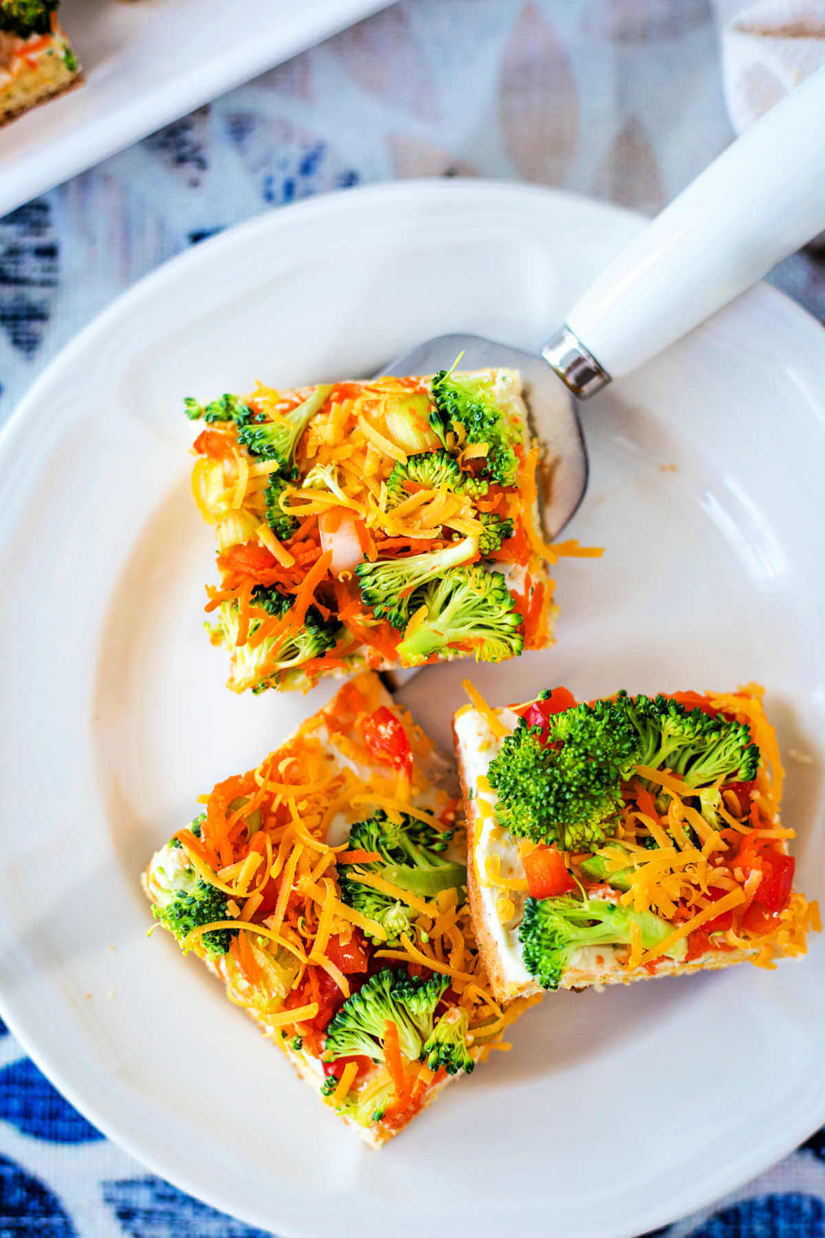 Three slices of crescent roll veggie pizza on a plate with a spatula.