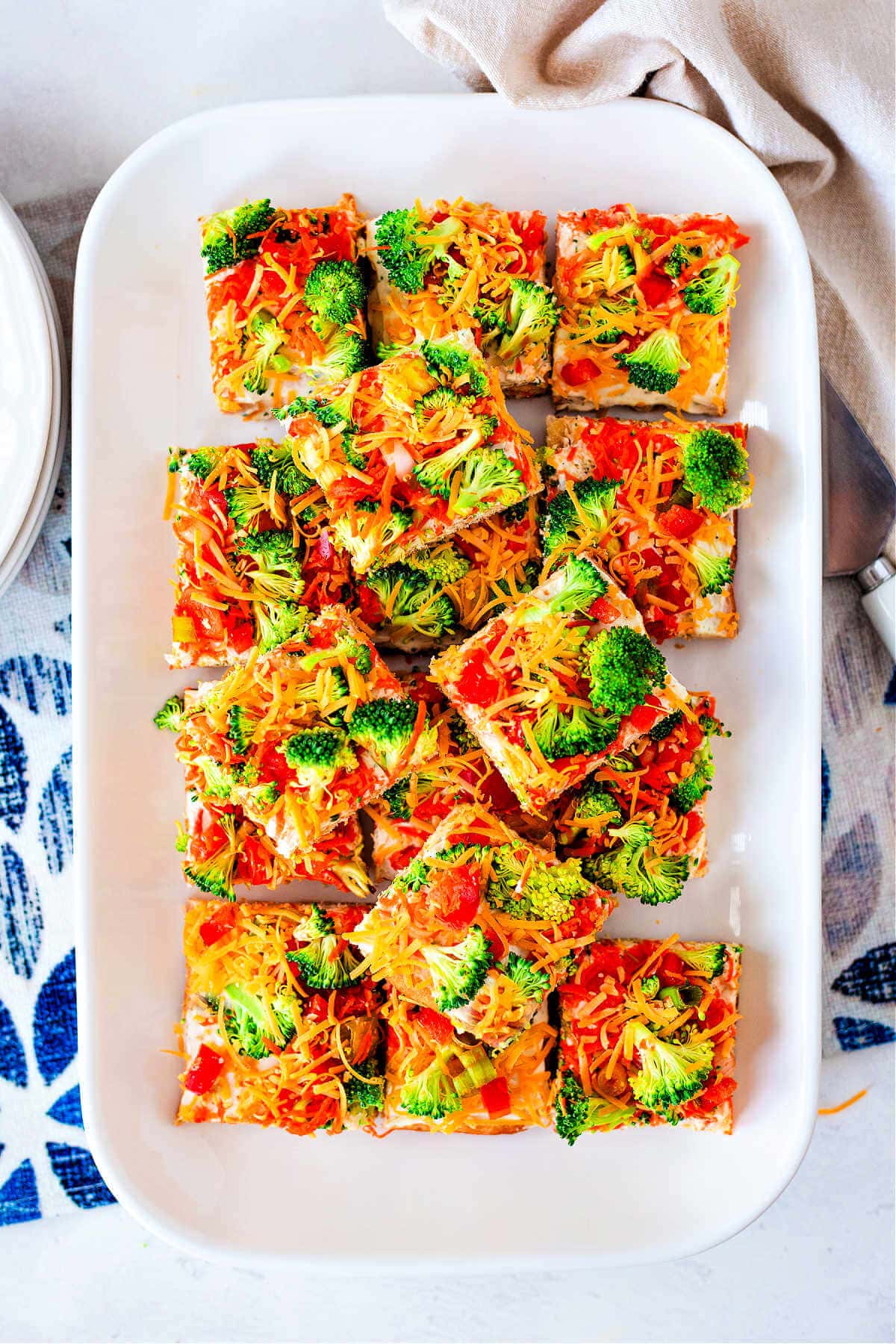 Square slices of crescent roll veggie pizza served on a white serving platter.