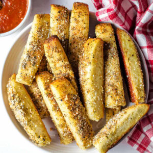 Cheesy Garlic Breadsticks on a plate with a bowl of marinara to the side.