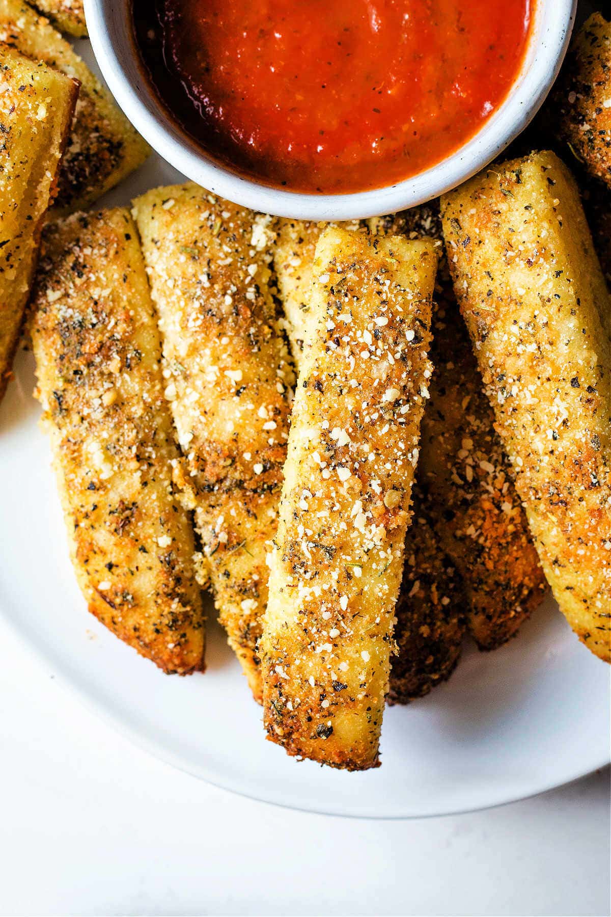Close up of parmesan garlic breadsticks served on a plate next to red sauce.