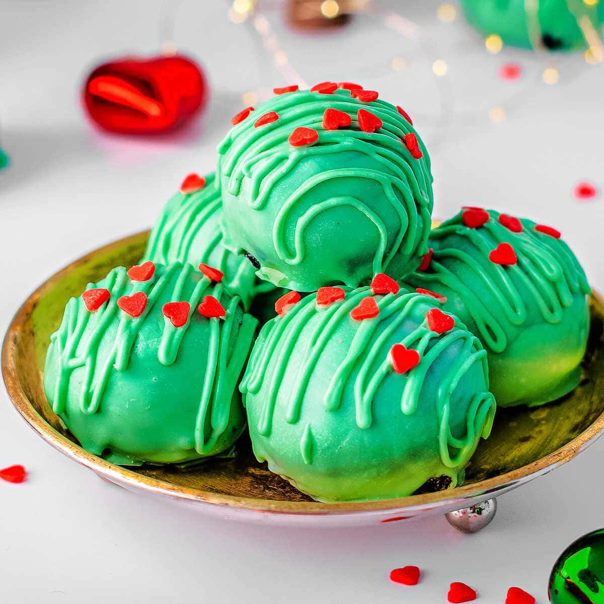 Oreo Balls decorated with green candy coating and red hearts for Grinch Oreo Balls.