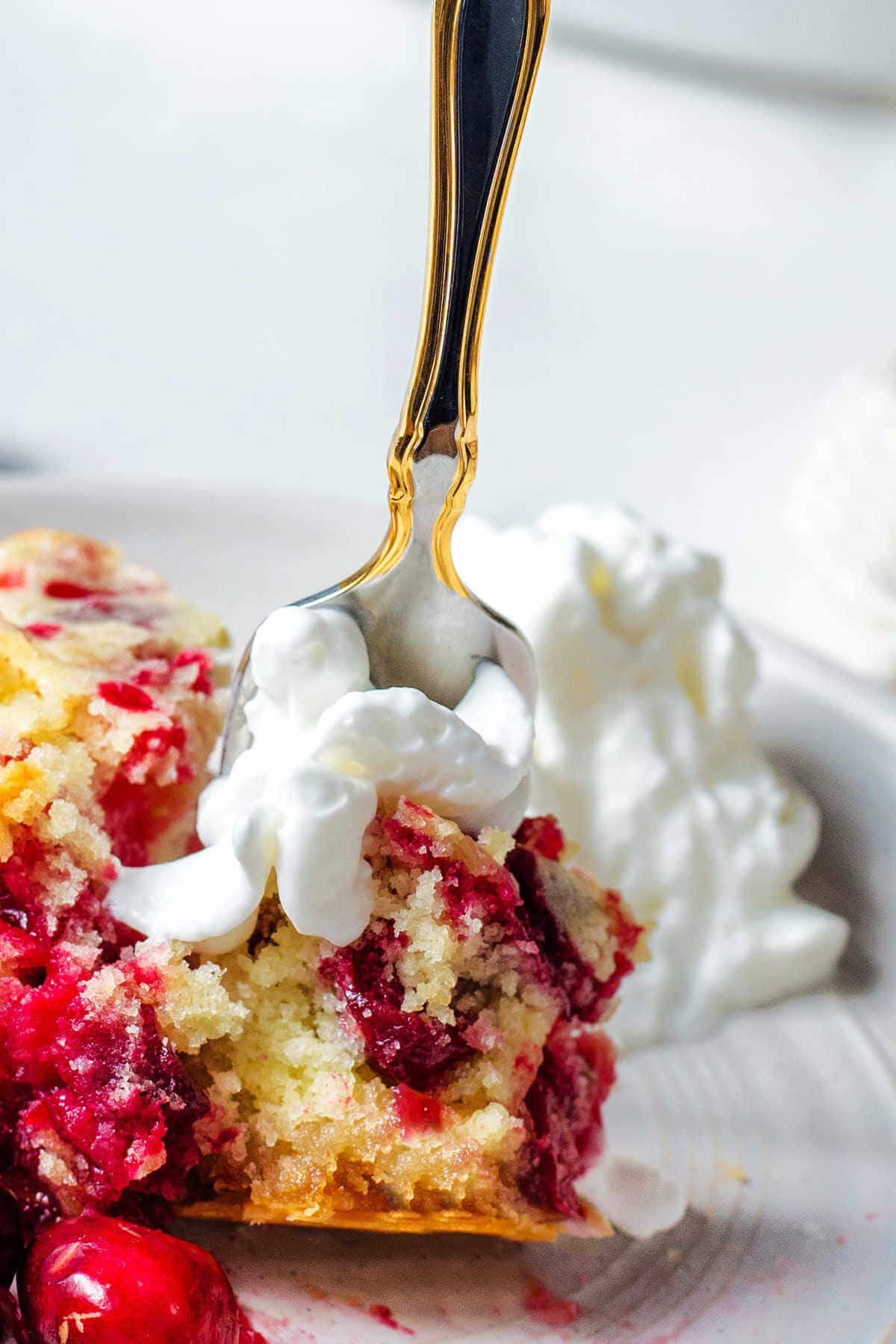 Close up of a fork taking a bite of cranberry pie with whipped cream.
