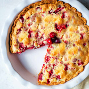 Overhead shot of a cranberry pie in a pie dish with a slice missing.