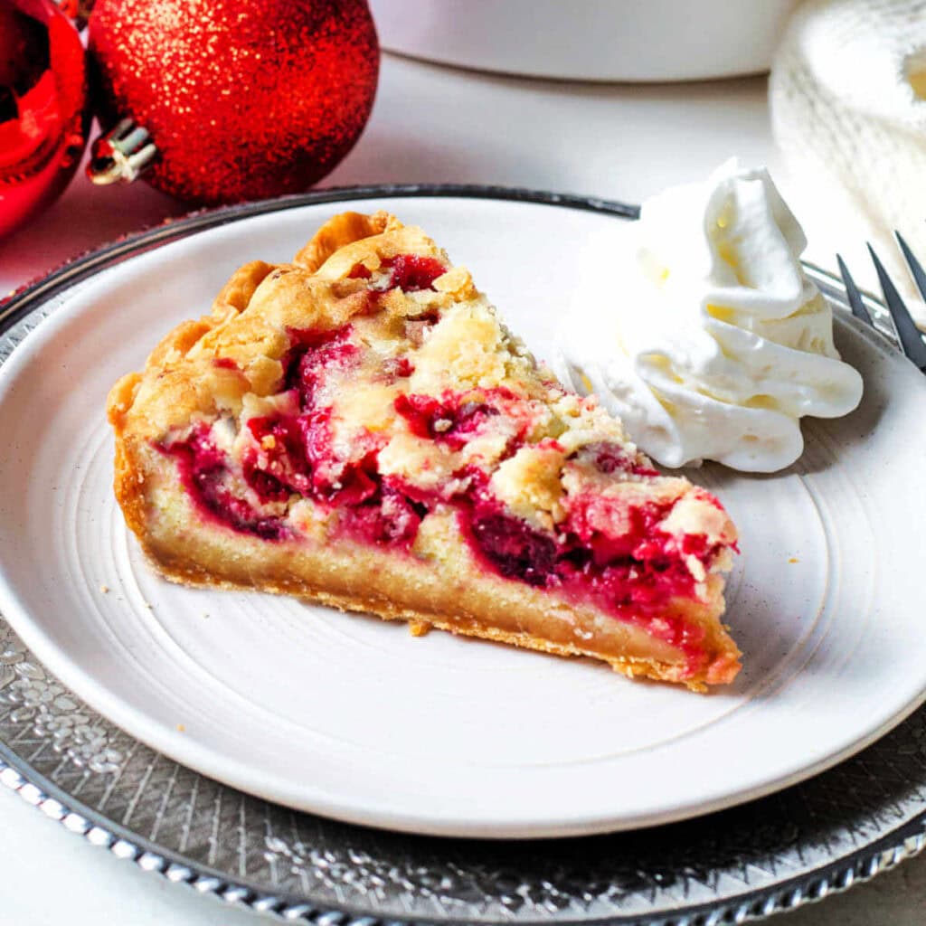 A slice of cranberry pie o a plate with whipped cream.
