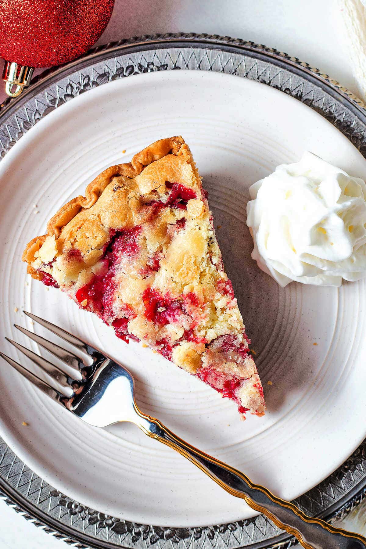 Overhead shot of a slice of cranberry pie on a plate next to whipped cream.