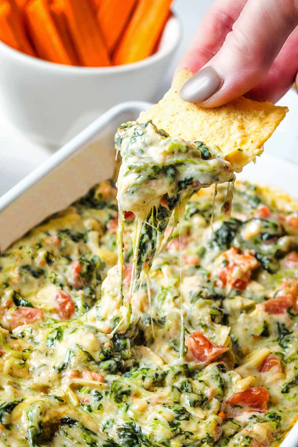 Hand dipping a tortilla chip into the spinach artichoke dip.
