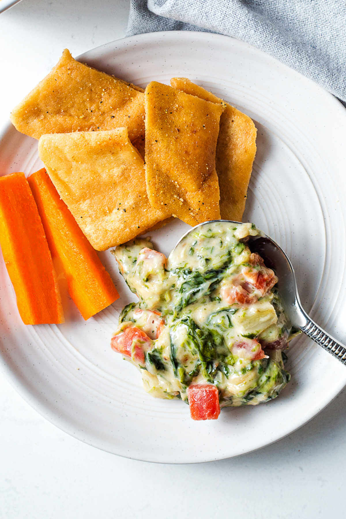 Spinach artichoke dip on a plate with pita chips and carrots on the side.