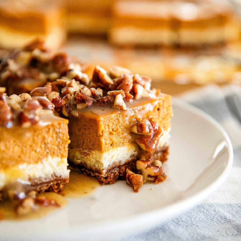 Pumpkin Cheesecake Bars drizzled with caramel pecan sauce on a plate.