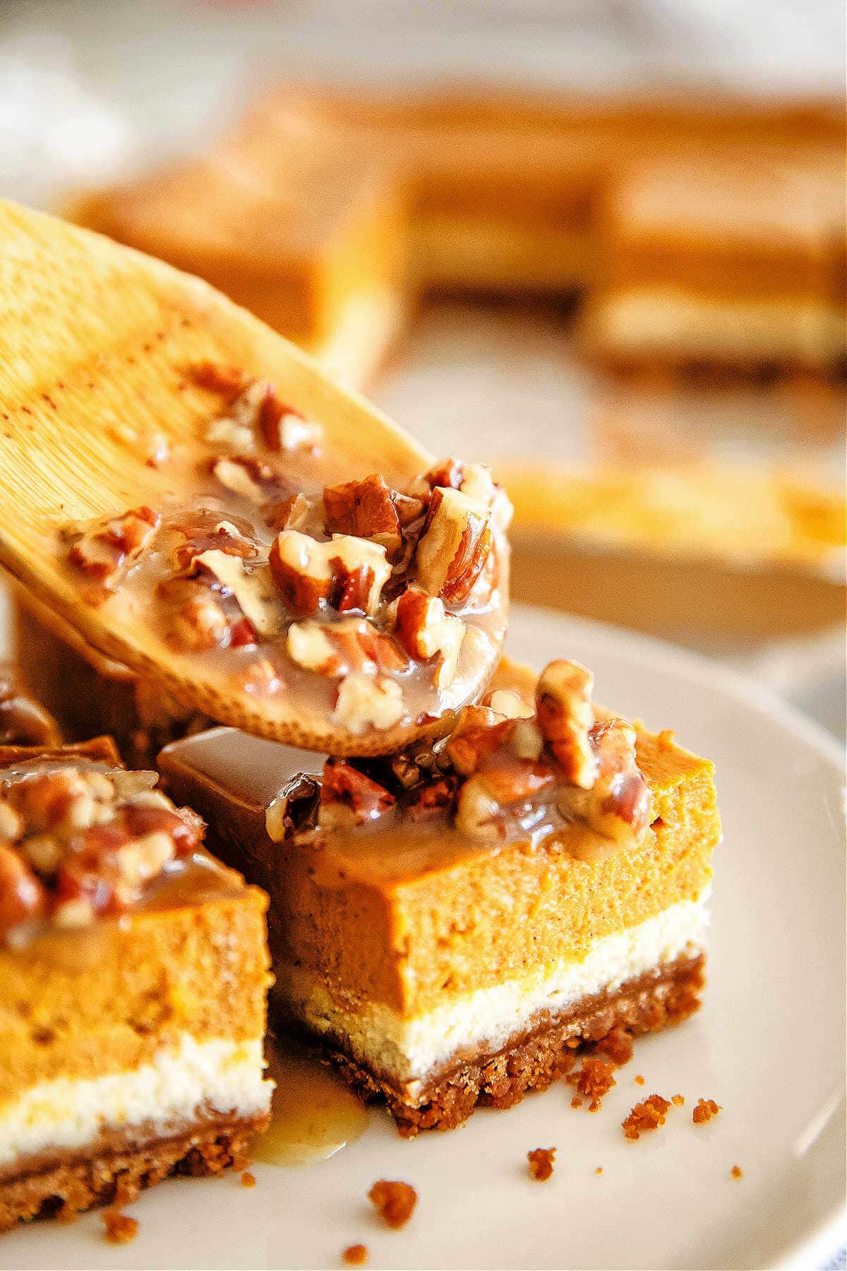 Spooning the pecan caramel sauce on top of the pumpkin cheesecake bars.
