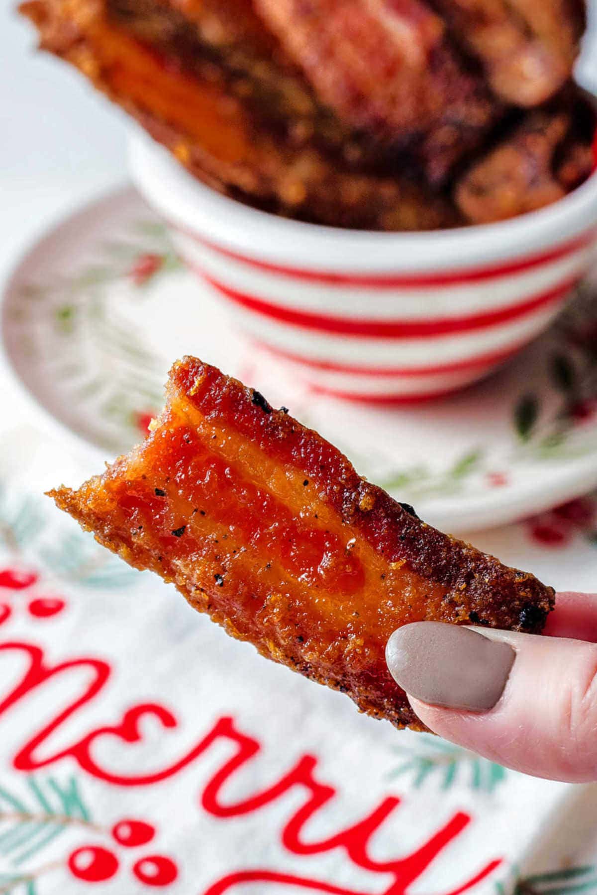 Hand holding a piece of candied bacon with a bite missing from the bacon.