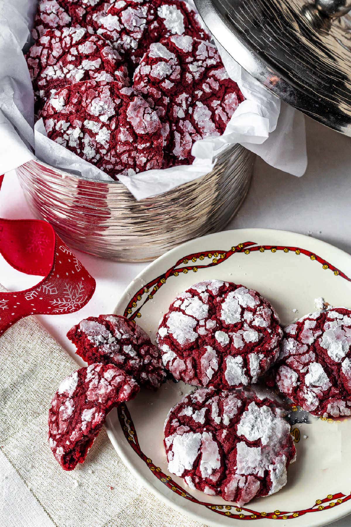Three red velvet crinkle cookies on a plate with more in a basket behind them.