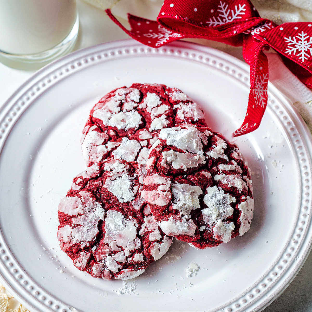 Three red velvet crinkle cookies on a white plate leaning on each other.