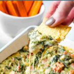Dipping a tortilla chips into a bowl of Easy Spinach Artichoke Dip.