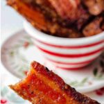 Hand holding a piece of candied bacon with a bite missing from the bacon.