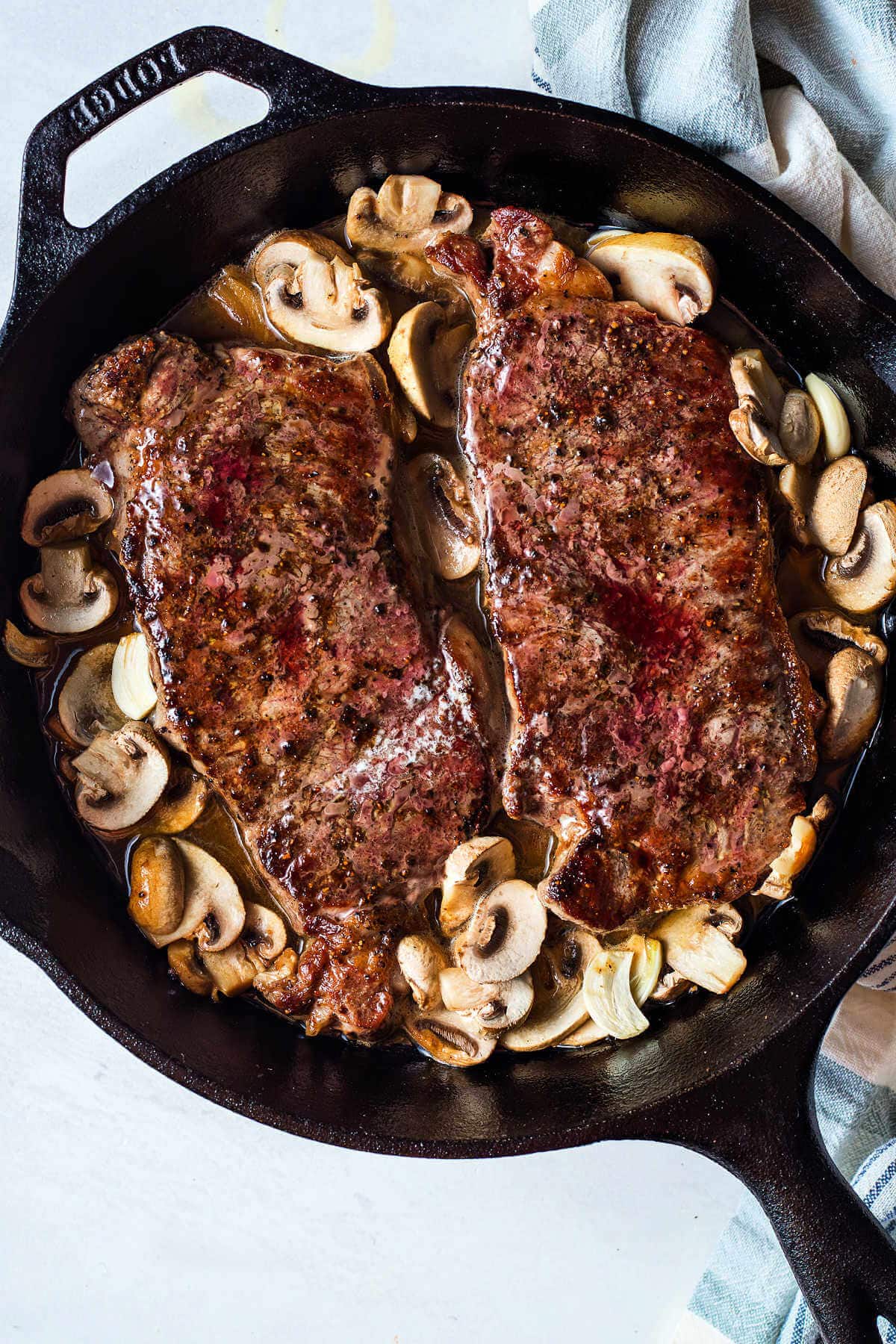 Two New York strip steaks in a cast iron pan straight out of the oven.