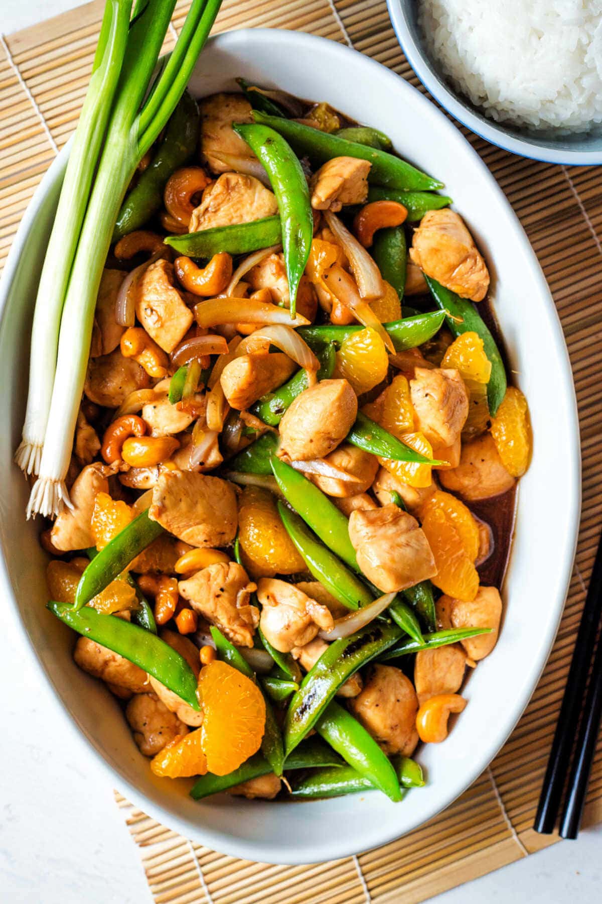 Chicken and cashew stir fry served in a large serving dish next to a bowl of rice.