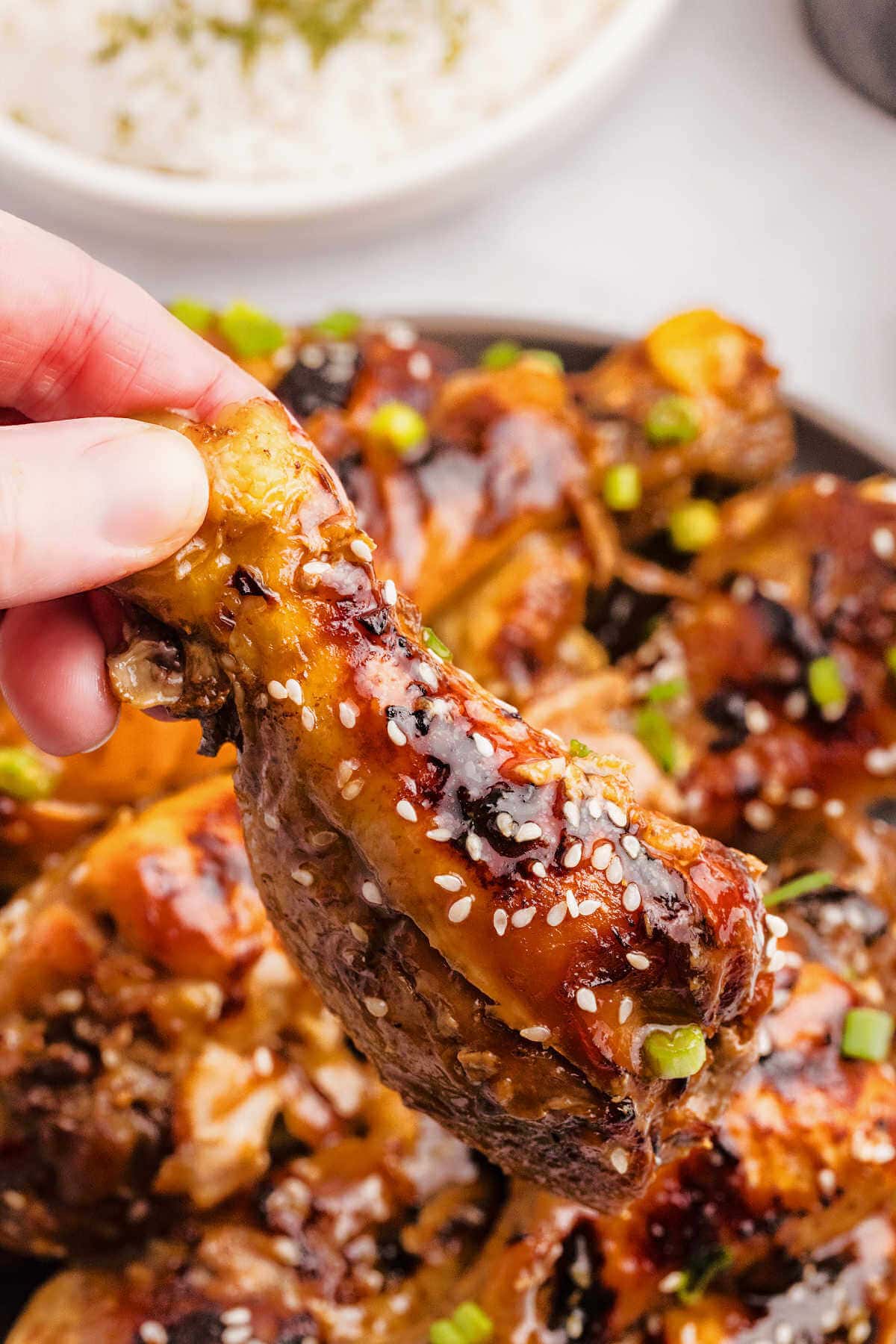 A hand lifting up a slow cooker chicken leg from a plate.