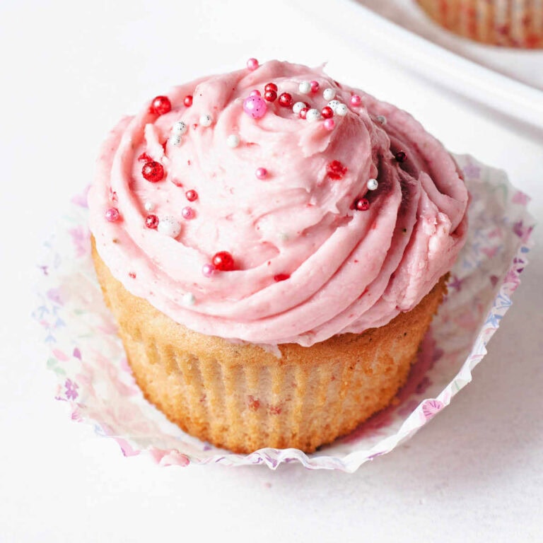 Close up of a strawberry cupcake with frosting and sprinkles on top.