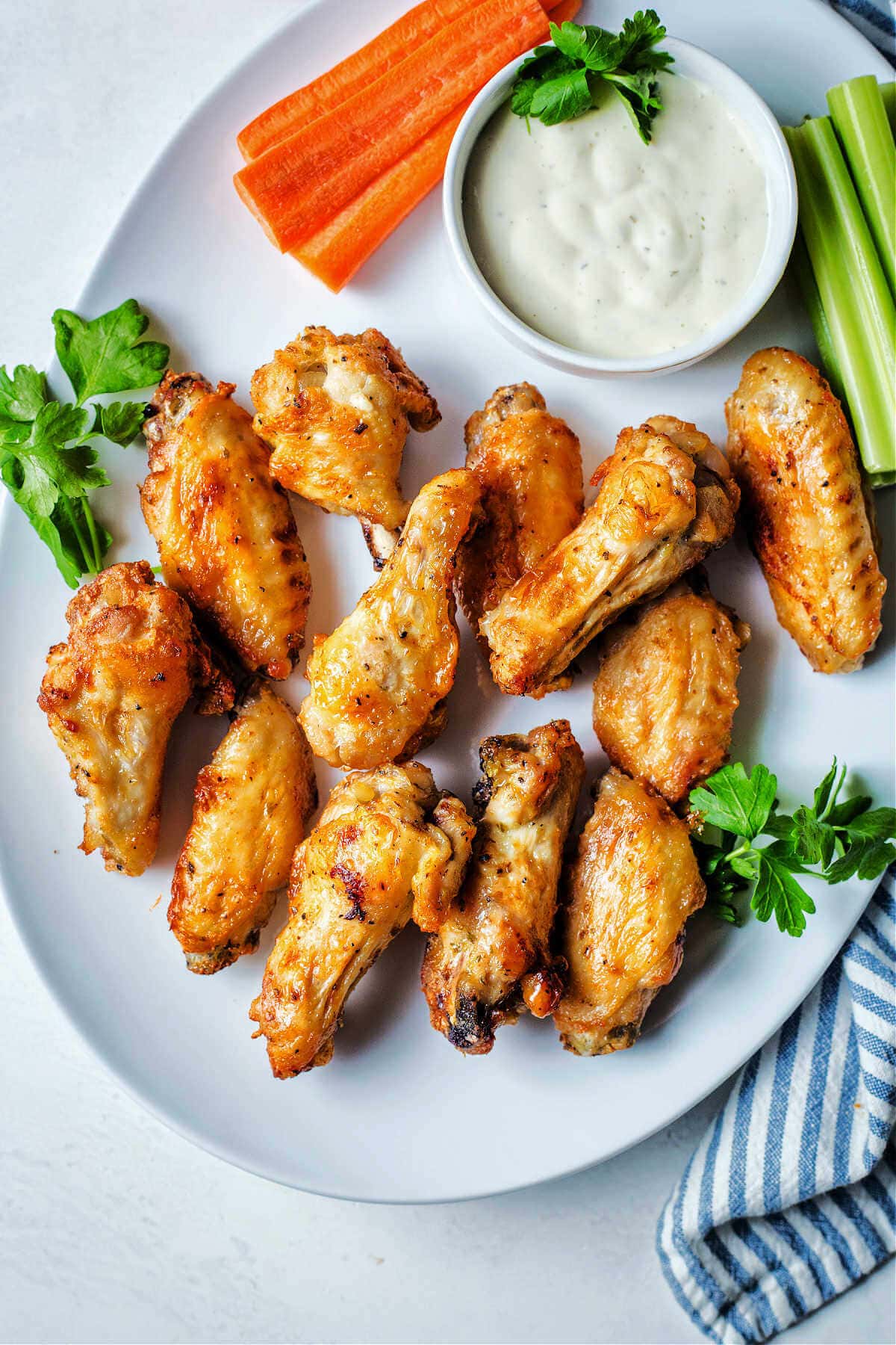 Air fryer chicken wings served on a plate with ranch and veggies.