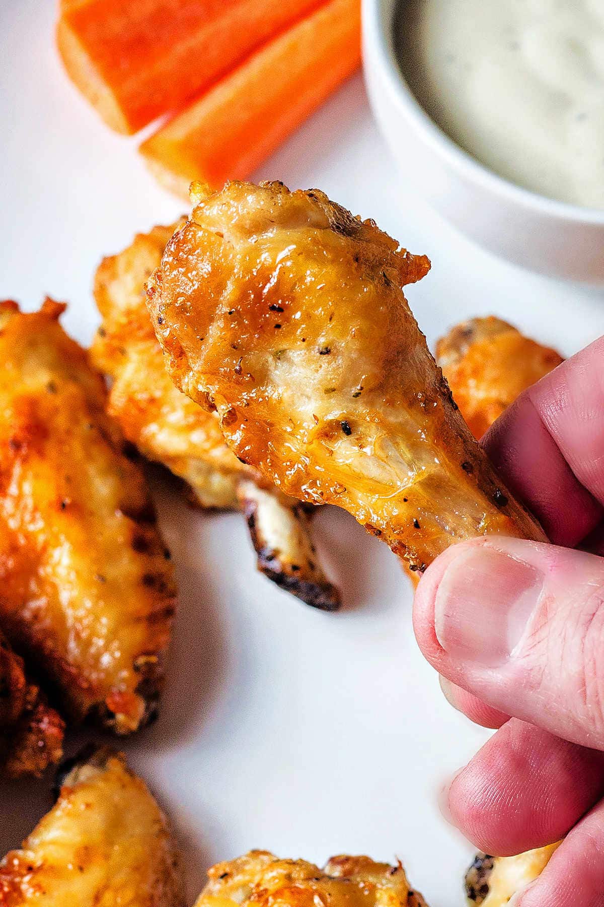 Hand holding an air fryer chicken wing hovering over a platter of wings.