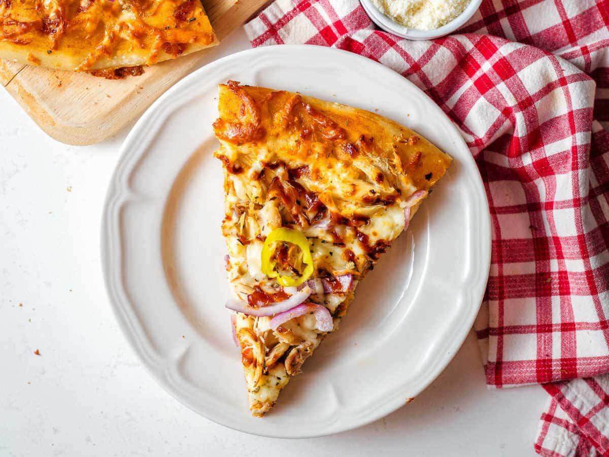 A slice of BBQ Chicken Pizza on a plate on a table with a red napkin.