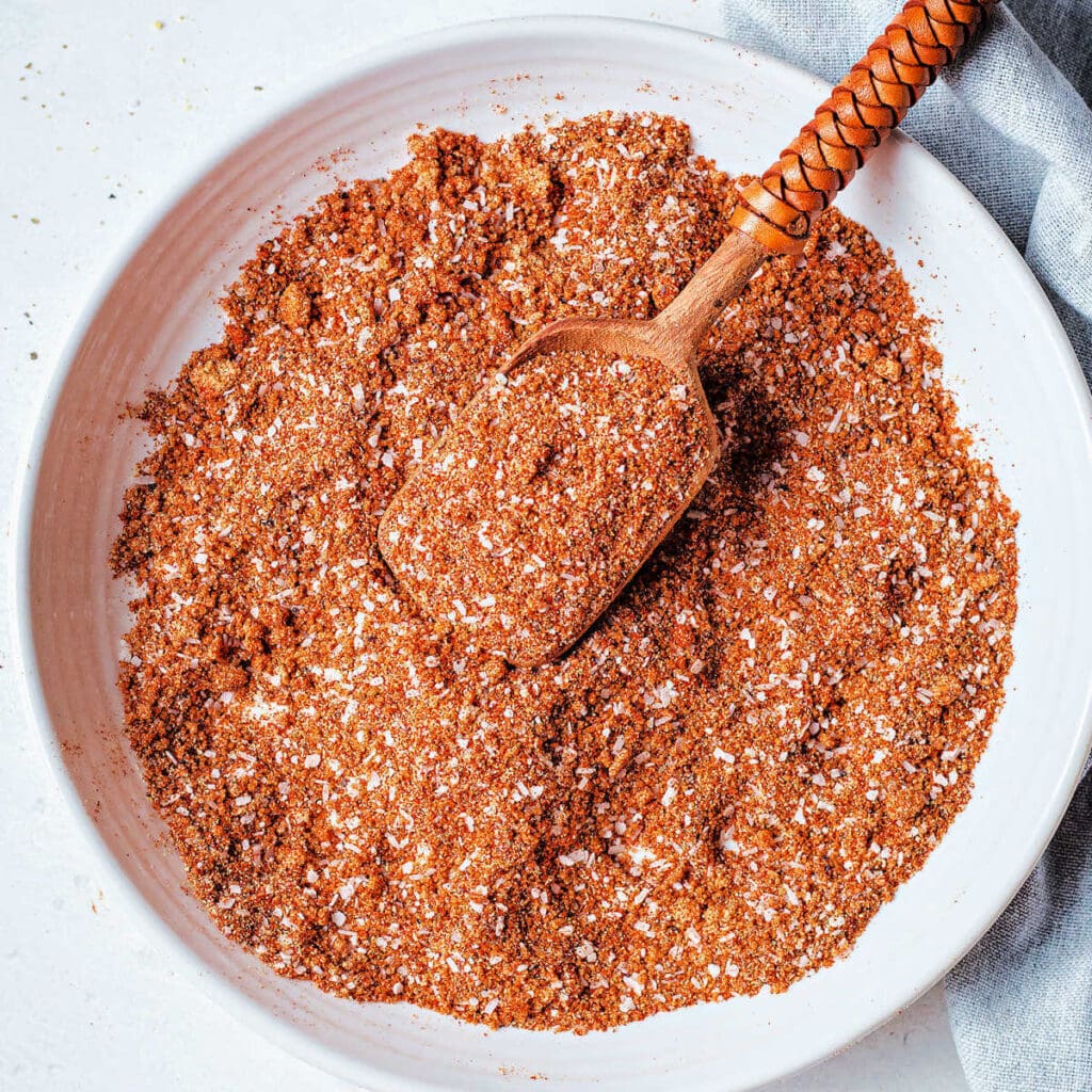 A mixture of spices for pulled pork spice rub in a bowl with a wooden spoon.