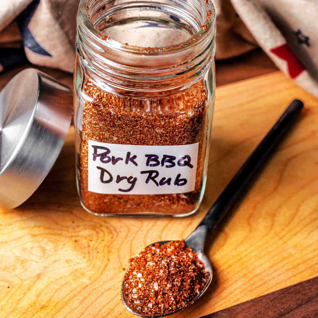 A mixture of spices for pulled pork spice rub in a glass jar.