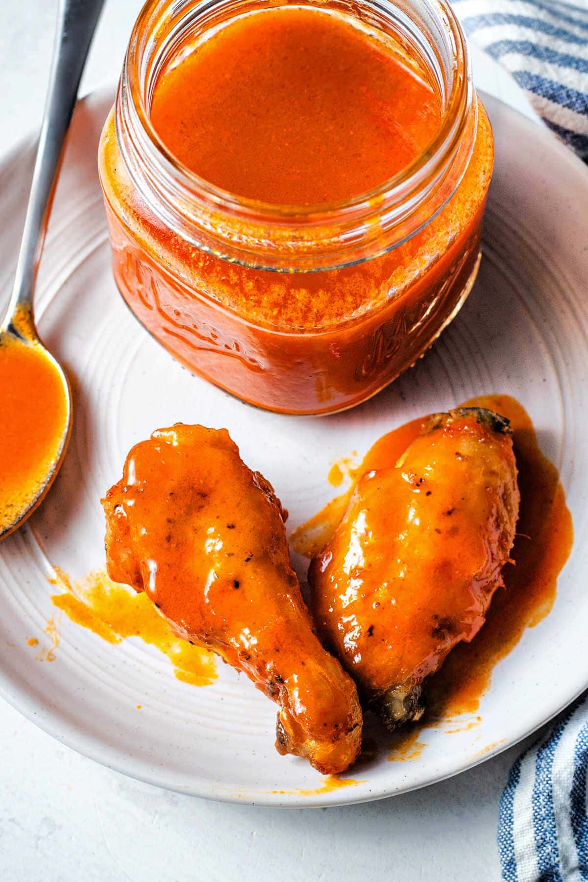 Two chicken wings on a plate covered in buffalo sauce next to a jar of buffalo wing sauce.