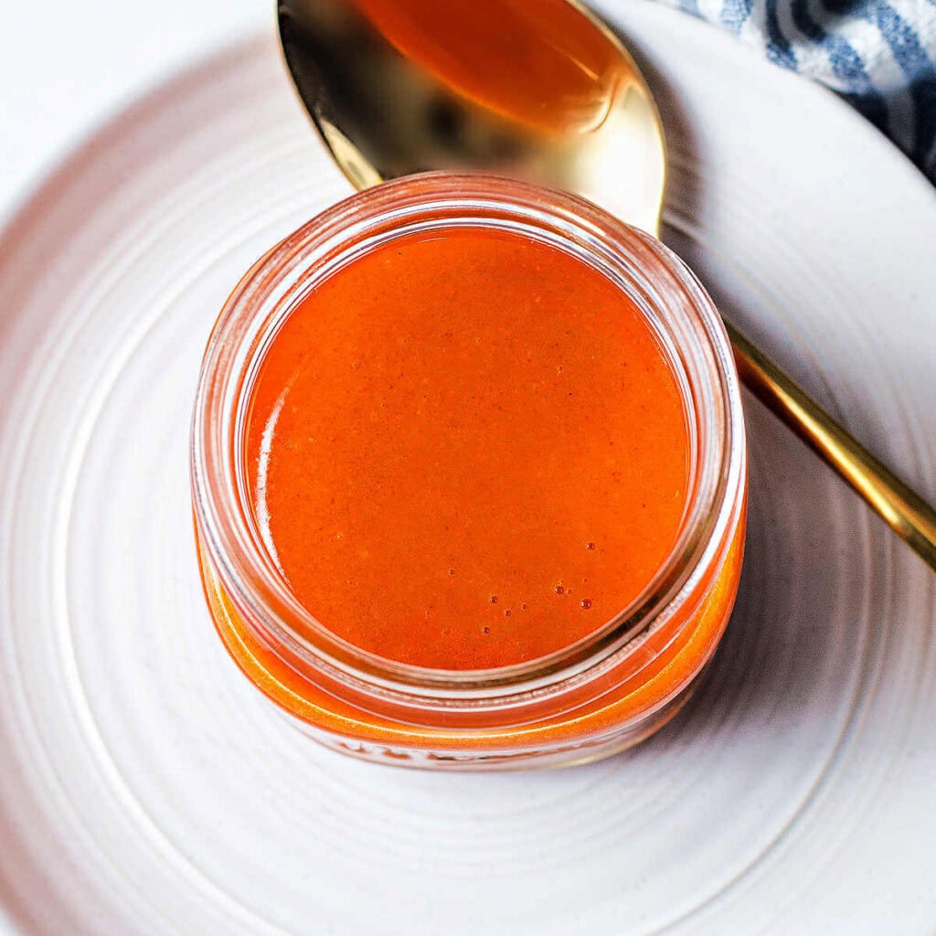 Buffalo Chicken Wing Sauce in a jar with a spoon on a plate.