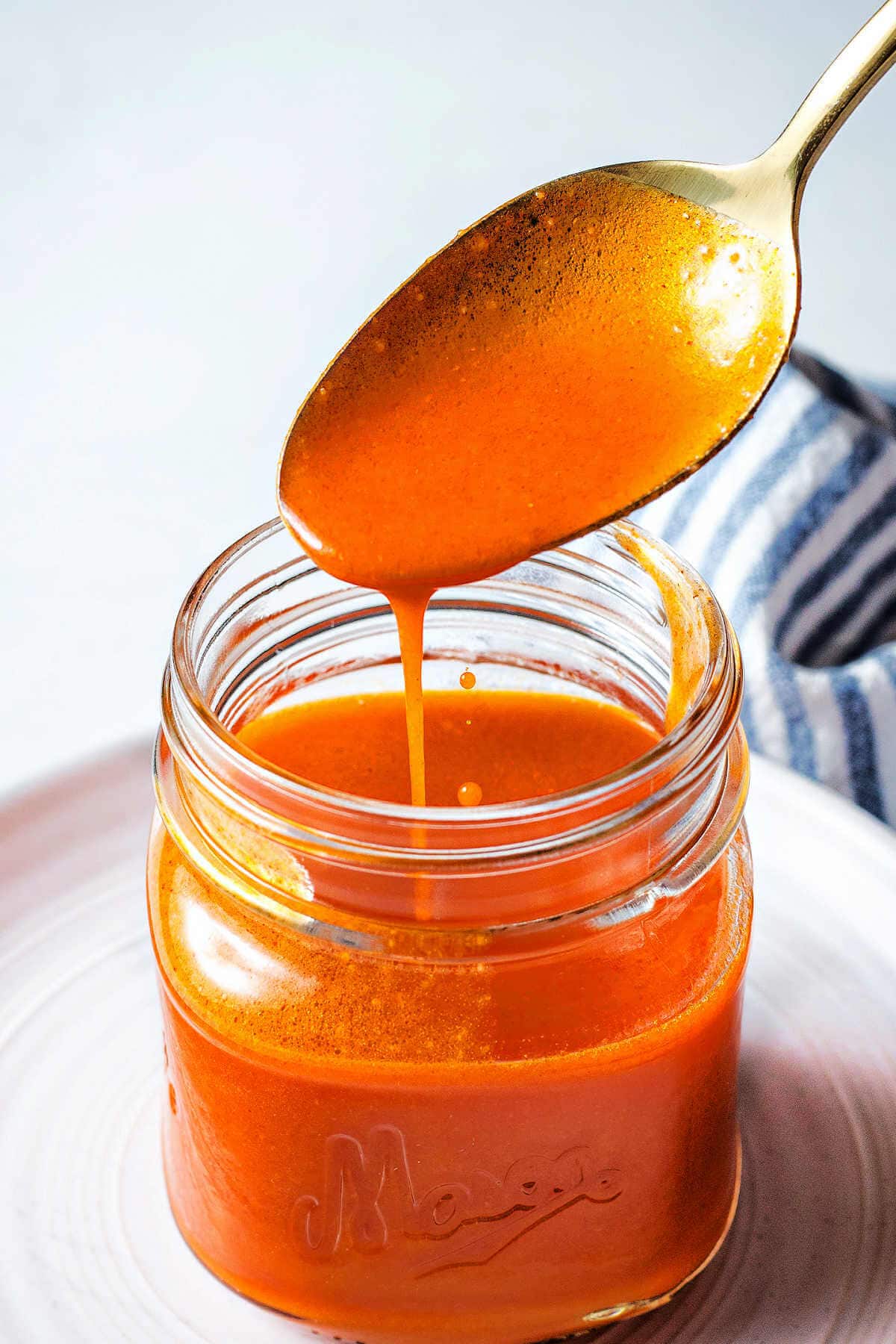 Finished buffalo chicken wing sauce in a jar with a spoon scooping some up.